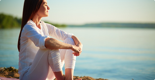 Frau sitzt entspannt an Gewässer im Sonnenlicht